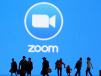 Small toy figures are seen in front of diplayed Zoom logo