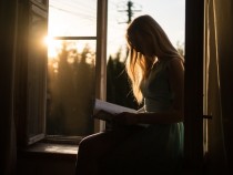 Woman reading book while sitting on windowsill
